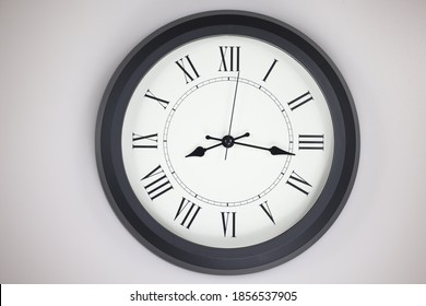 Close-up of a  old-fashioned antiquated wall clock with roman numerals on the clock face. Clock with black frame on a white background. Antique pointers showing the time.  front view of the watch 