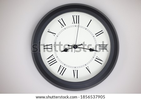 Close-up of a  old-fashioned antiquated wall clock with roman numerals on the clock face. Clock with black frame on a white background. Antique pointers showing the time.  front view of the watch 