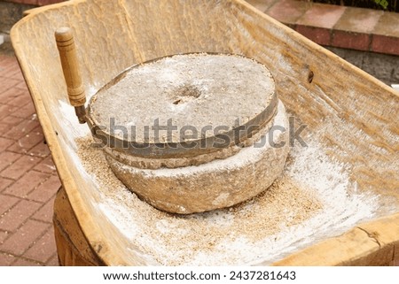 A close-up of an old-fashioned stone mill used for grinding grains, positioned on a wooden table with residues of flour.