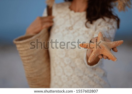 Closeup on 40 year old woman in white dress and straw hat on the seashore at sunset showing starfish.