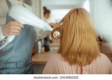 Closeup on 40 years old woman hairdresser in modern beauty salon with hairbrush and client blowout hair with hair dryer. - Powered by Shutterstock