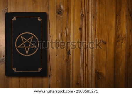 Close-up on a black book with a gilded Reverse Pentagram on a brown woodboard.