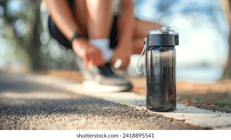 Closeup on black bottle of water, Blurred man tie their shoes before run on track race in the public park, Healthy - Powered by Shutterstock