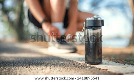 Closeup on black bottle of water, Blurred man tie their shoes before run on track race in the public park, Healthy