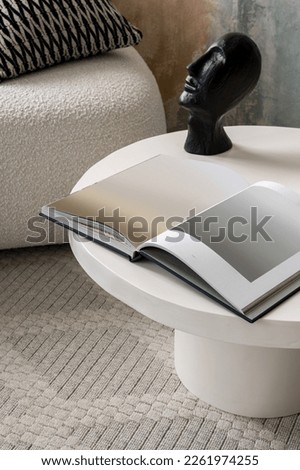 Close-up on black sculpture and album with art on stone and modern coffee table in room with beige carpet