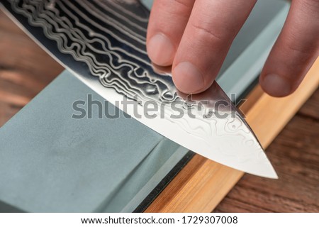 Close-up on a blade made of Damascus steel. Man using a whetstone to sharpen a Japanese chef's knife.