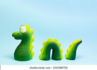 Close-up On Blue Background Of Decorative Toy Characterized As Loch Ness Monster, Pretending To Have Part Of His Body Submerged On The Support On Which It Rests.