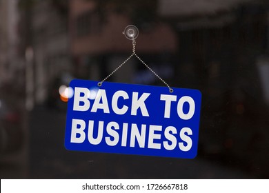 Close-up on a blue open sign in the window of a shop displaying the message "Back to business".