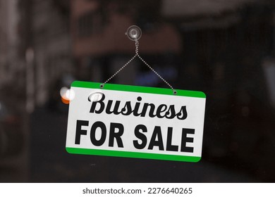 Close-up on a blue open sign in the window of a shop displaying the message: Business for sale.
