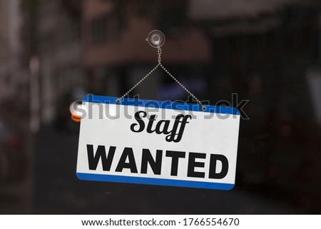Close-up on a blue open sign in the window of a shop displaying the message: Staff wanted.
