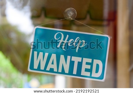 Close-up on a blue sign in the window of a shop displaying the message - Help wanted -.
