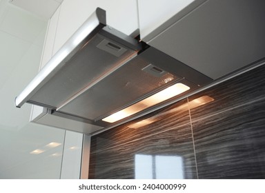 A close-up on a built in, integrated into kitchen cabinet stainless steel range hood, cooker hood, exhaust or extractor vent hood working with lights on in the kitchen.
