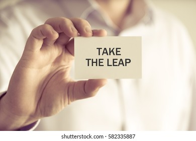 Closeup On Businessman Holding A Card With Text TAKE THE LEAP, Business Concept Image With Soft Focus Background And Vintage Tone
