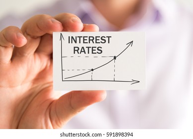 Closeup on businessman holding a card with INTEREST RATES rising arrow and chart, business concept image with soft focus background