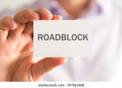 Closeup On Businessman Holding A Card With ROADBLOCK Message, Business Concept Image With Soft Focus Background