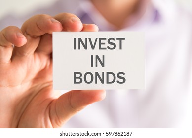 Closeup on businessman holding a card with INVEST IN BONDS message, business concept image with soft focus background