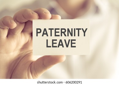 Closeup on businessman holding a card with text PATERNITY LEAVE, business concept image with soft focus background and vintage tone