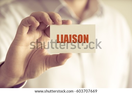 Closeup on businessman holding a card with text LIAISON , business concept image with soft focus background and vintage tone