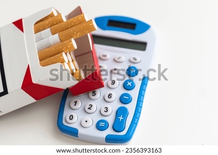 closeup on calculator with digits on display, cigarette pack and lighter on white background, smoking expenses concept
