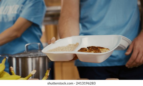 Close-up on caucasian man serving bread chicken and baked beans to poor hungry person at food drive. Detailed view of meal box from hunger relief team given to the needy. Selective-focus handheld.