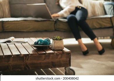 Closeup On Coffee Table And Young Woman Using Laptop In Background