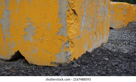 Closeup On Concrete Traffic Barrier. Ciment Blocks Painted In Yellow In Row On Black Gravel. Wheel Stop On Parking. Road. Construction. - 2 June 2022, Montreal, Canada