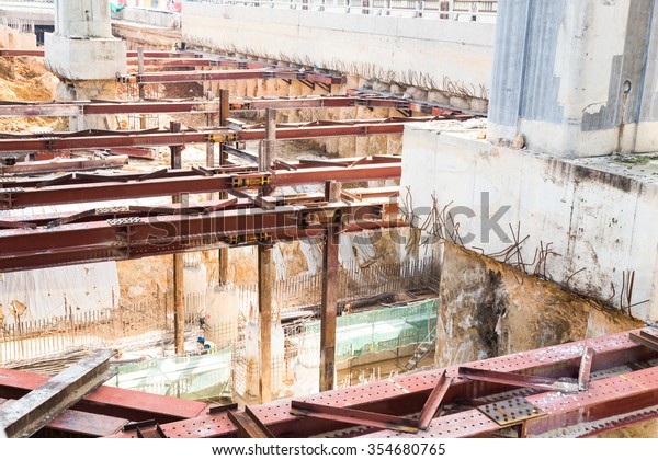 Closeup on construction of\
tunnel underpass underway with metal beams and huge pillar beneath\
train line