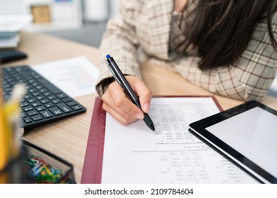 Close-up on a document, statistical table, company's calculations, an office accountant sits at the desk filling in the right places, checking the correctness, touches the paper with a pen