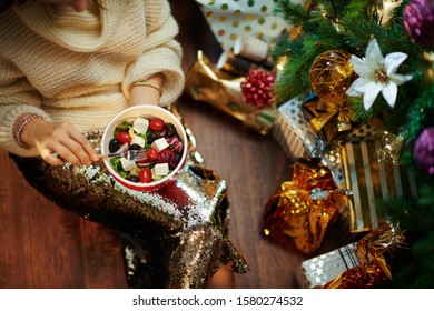 Closeup On Elegant 40 Year Old Woman In Gold Sequin Skirt And White Sweater Under Decorated Christmas Tree Near Present Boxes Eating Healthy Salad.