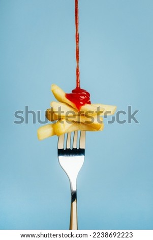close-up on french fries with pouring ketchup on a fork on a blue background