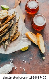 Close-up On Fried Fish Anchovy With Beer In Glasses Next To Bread, Lemon, Salt On A Concrete Background