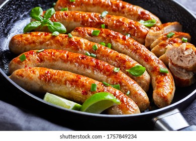 Close-up On A Fried Pork Sausage Links Of Minced Meat Served On A Skillet With Fresh Basil And Spring Onion On Top, Lime Wedges, On A Dark Wooden Table