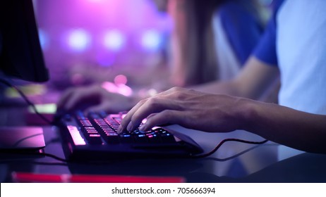 Close-up On Gamer's Hands on a keyboard, Actively Pushing Buttons, Playing MMO Games Online. Background is Lit with Neon Lights.