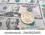 Close-up on a golden Monero coin on top of a stack of US Dollar banknotes.