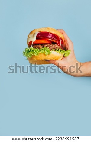 close-up on a hamburger in a female hand on a blue background