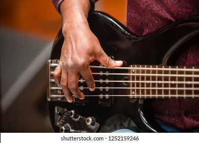 Close-up On Hand Of African American Bass Player, Fingers On Black Five String Electric Bass Guitar.