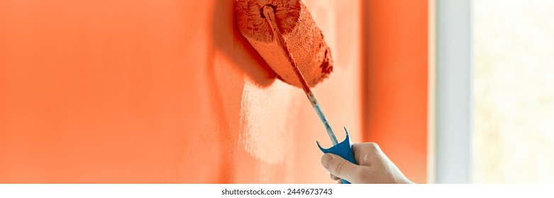 Close-up on the hand of a man who is painting a wall red orange with a paint roller. Painting apartment, renovating with red orange color paint. - Powered by Shutterstock