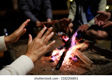 Close-up on hand of woman warming on campfire. Group of asian friends sitting around campfire in the night. Friends camping near bonfire relaxing on winter vacation at the night time. - Shutterstock ID 2182206851