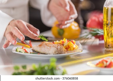 closeup on the hands of a chef in a professional kitchen carefully depositing a sprig of dill on a cod fillet - Shutterstock ID 376060858