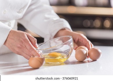 close-up on the hands of a chef in a professional kitchen holding a bowl and braking eggs - Powered by Shutterstock