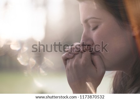 Close-up on hands and face of sad young woman with anxiety against blurred background