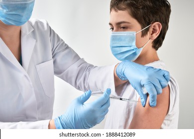 Close-up on hands in gloves with syringe and shoulder of the patient, teen kid. Covid 19, flu, tetanus or measles vaccine concept. Unrecognizable edic, doctor or nurse vaccinates school boy.