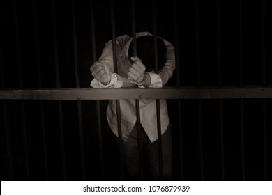 Closeup On Hands Of Man Sitting In Jail. Man Behind Jail Bars On Black Background