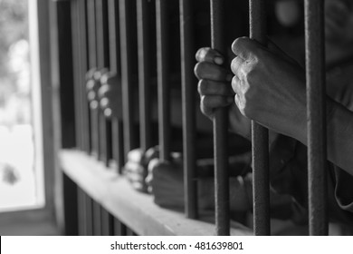 Closeup On Hands Of Man Sitting In Jail. Man Behind Jail Bars With Black And Wthite Style