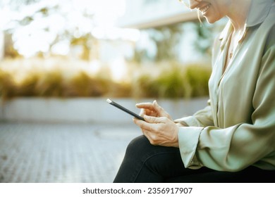 Closeup on happy female employee in business district in green blouse and eyeglasses with smartphone. - Powered by Shutterstock