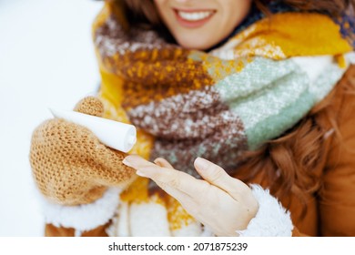 Closeup On Happy Woman In Brown Hat And Scarf With Mittens Using Hand Cream Outside In The City Park In Winter.