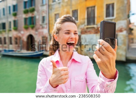 Closeup on happy young woman showing thumbs up and making selfie in venice, italy
