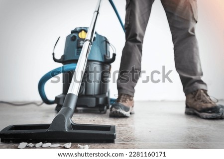 Close-up on the legs of a worker and the brush of a construction vacuum cleaner at a construction site.