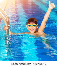 Closeup on little boy wearing swimming goggles in the pool, junior swimming competition, happy winner with raised up hand, summer time sport