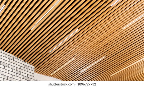 Close-up On A Loft-style Pine Wood Plank Ceiling Combined With White Brick Wall Trim. The Idea Of ​​a Ceiling Design In A Minimalist Style. Original LED Strip Lamps On The Wooden Ceiling.